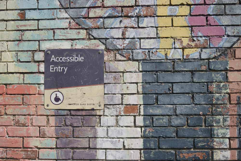 A brick walll with colourful paintings and a sign saying "Accessible entry"