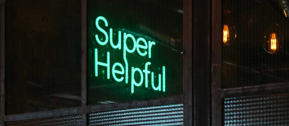 A green neon sign in a sans serif typeface saying "Super Helpful"
