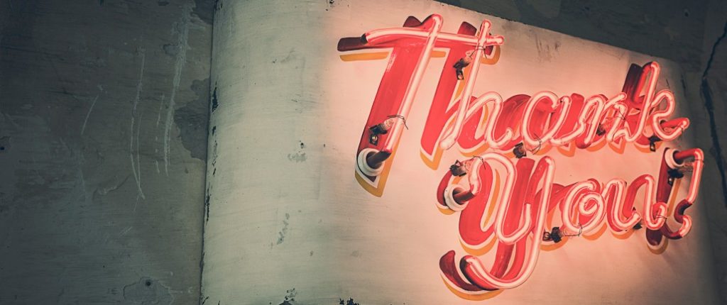 A neon sign in red cursive script on a wall, saying "Thank you"